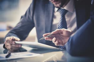 Image of two young businessmen using touchpad at meeting